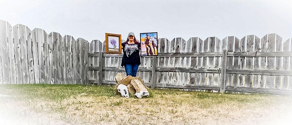 一个女人站在灰色的栅栏前，手里拿着两幅画